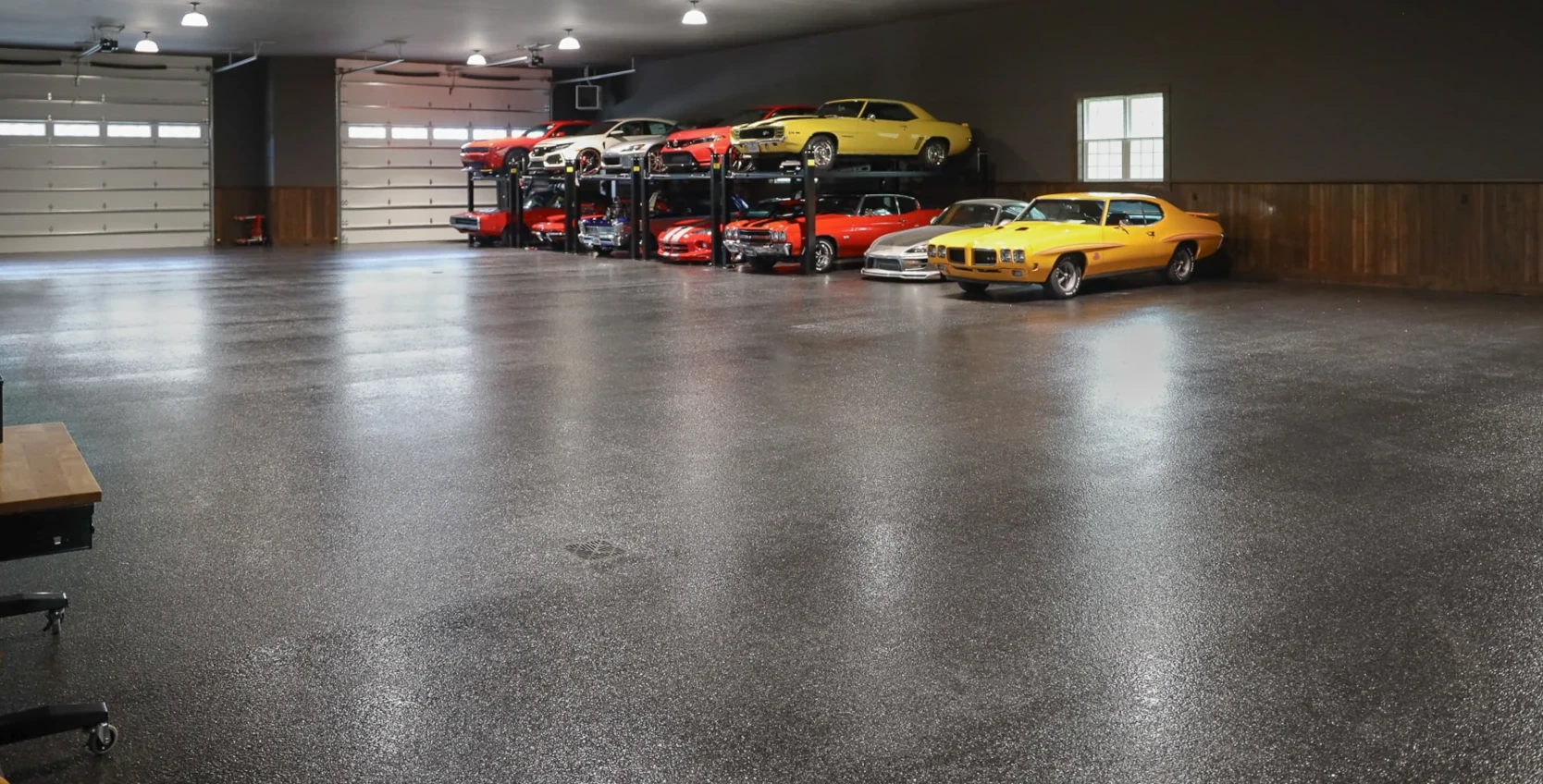 Wide-angle shot of a large residential garage in Massillon, OH with glossy polyaspartic flake flooring and classic cars on lifts.