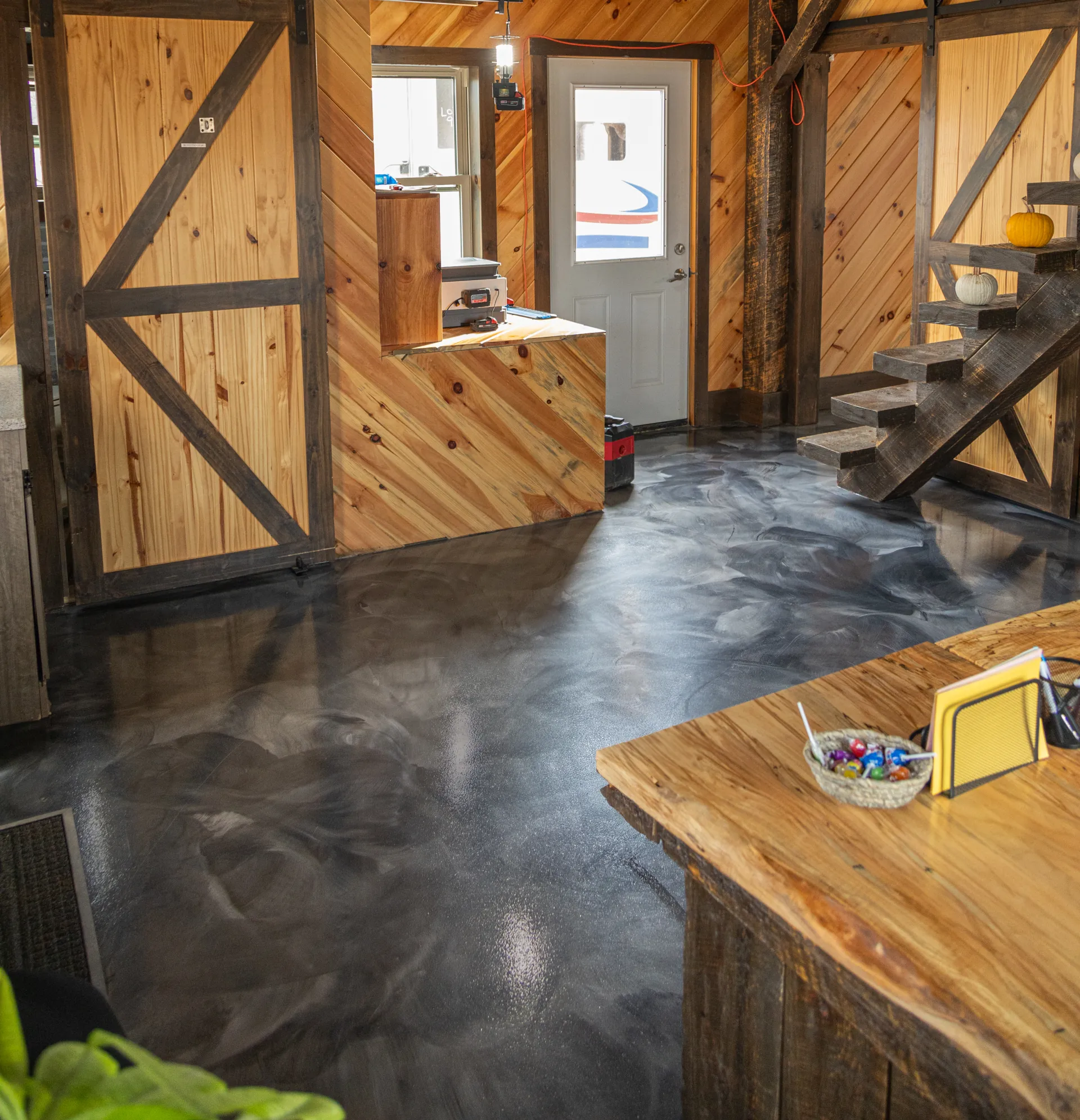 Reception area with rustic wood walls and stairs featuring a new silver and charcoal metallic epoxy floor at Miller Brothers Hardwood, Salesville Ohio.