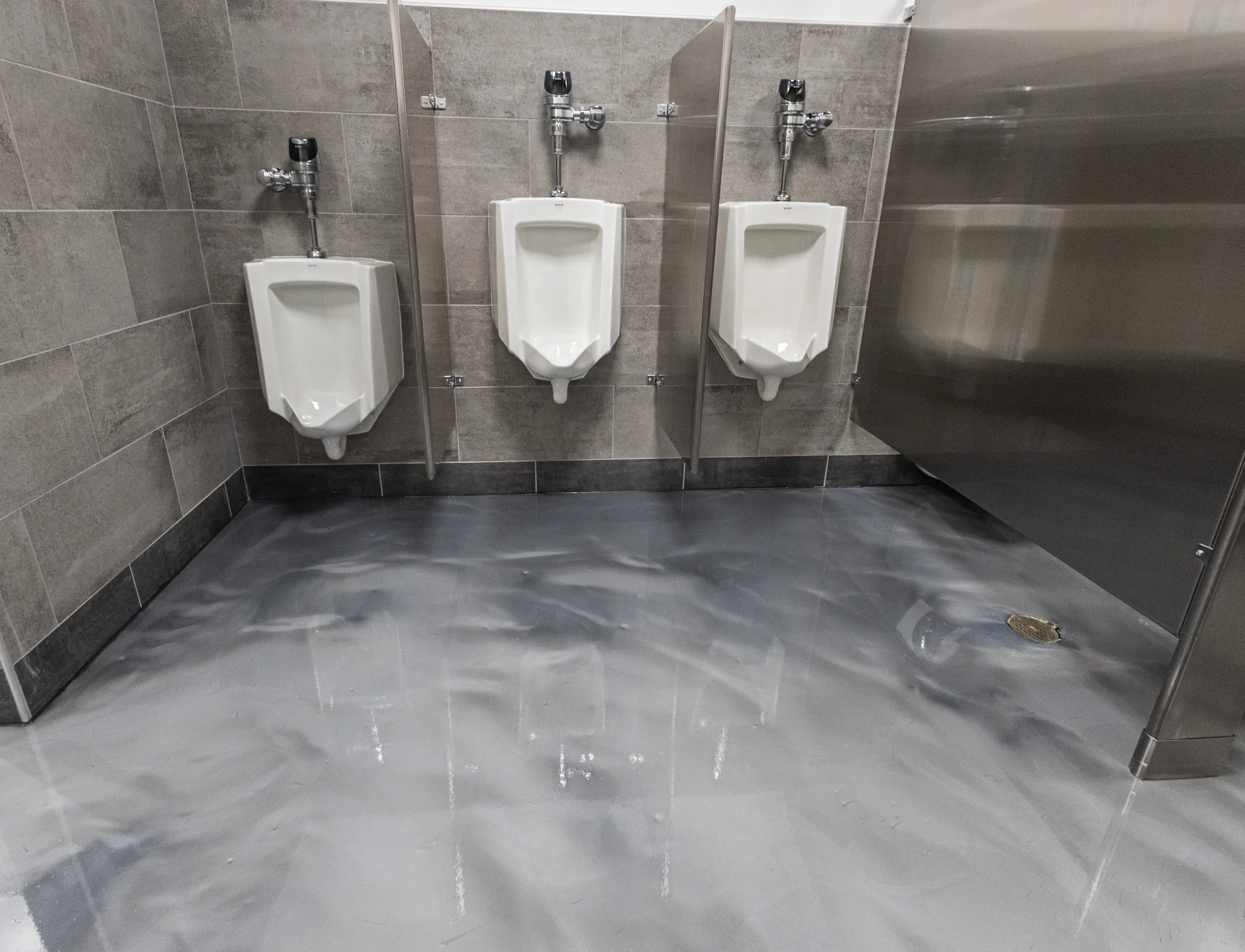 Metallic silver epoxy floor in a commercial restroom with gray wall tile and three urinals.