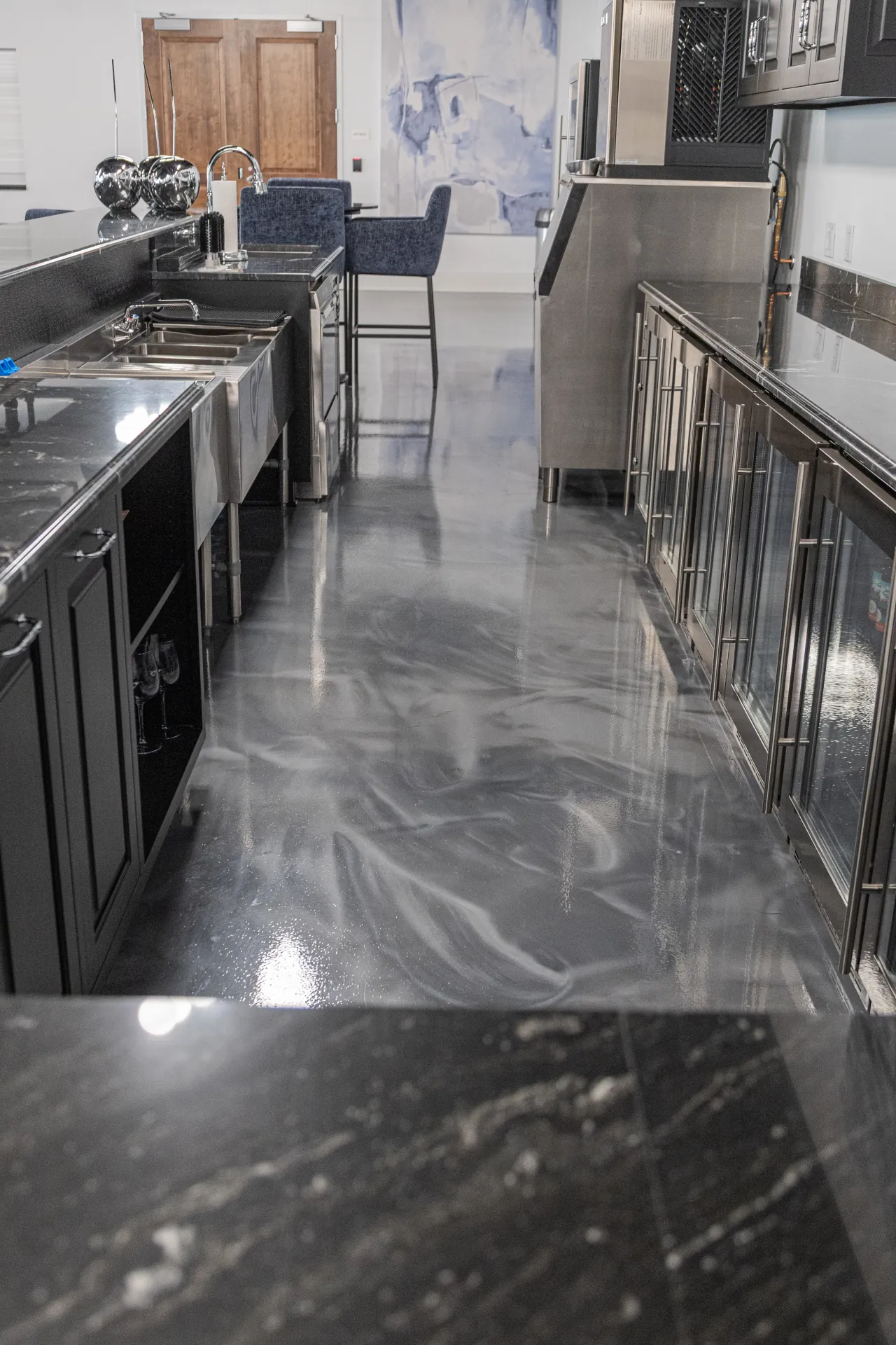 Sleek metallic epoxy walkway in a café/bar prep area with stainless equipment and dark cabinetry.