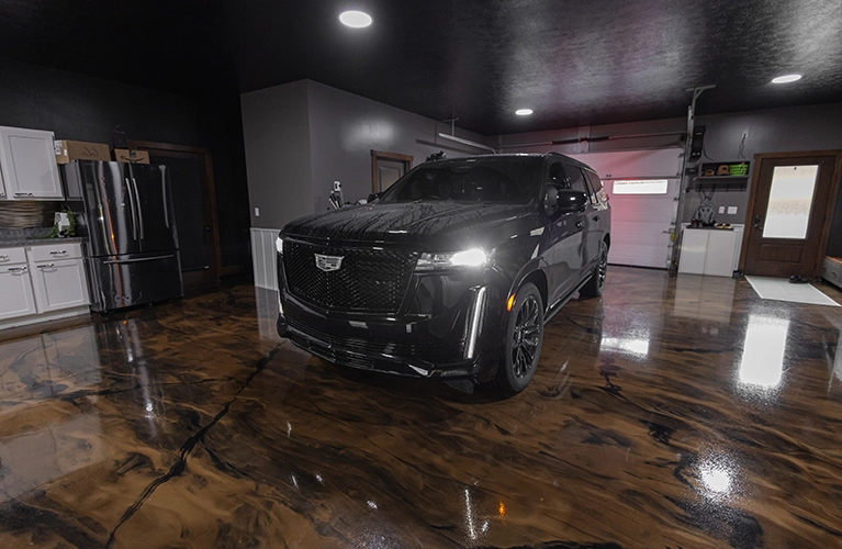 Front view of a black SUV in a modern garage with glossy epoxy floors, white cabinetry, and dark ceiling.