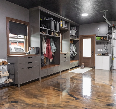 Modern garage interior with built-in storage cabinets, hanging coats, and a high-gloss metallic epoxy floor.