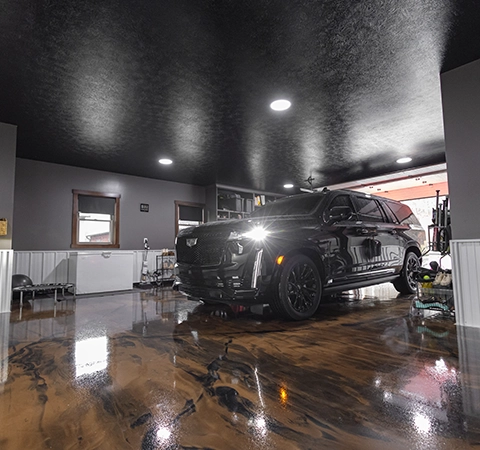 Black SUV parked inside a finished garage with polished metallic epoxy flooring and overhead lights.