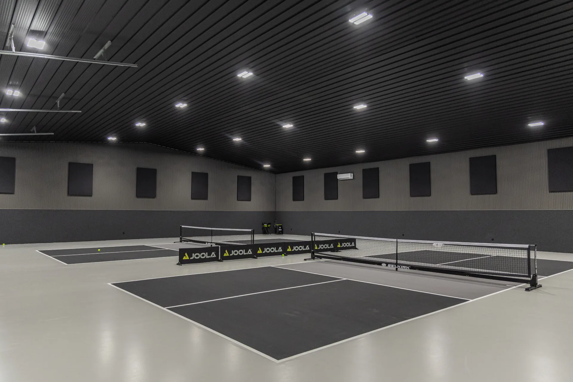 wide view of 2 pickleball courts in a warehouse. Black, white, and grey color finish.