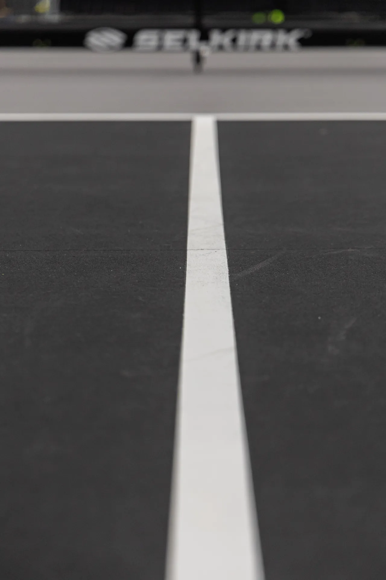 close up view of a white midline on a black pickleball court