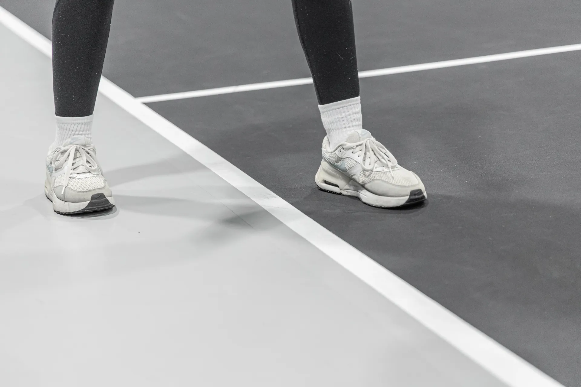 close up view of pickleball court sidelines, with a person standing overtop of the white line.