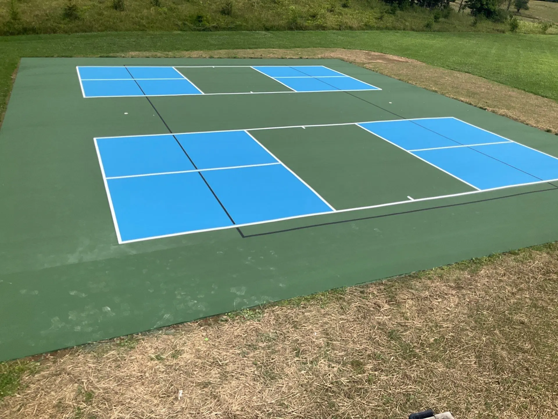 Finished outdoor pickleball courts with blue playing areas and green court coating