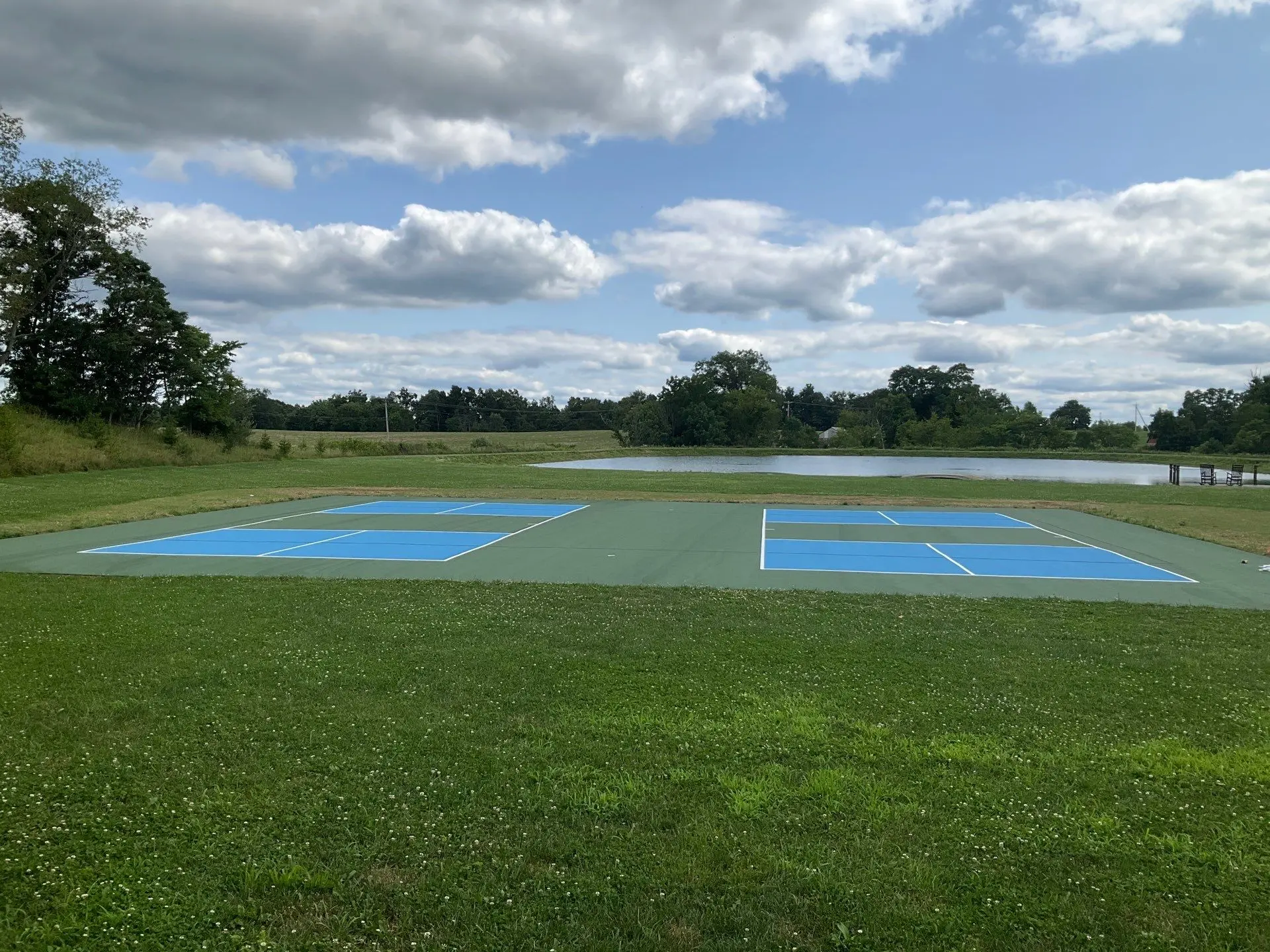 Outdoor pickleball court coating project overlooking a pond and grassy property