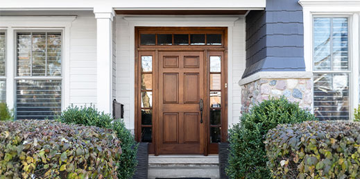 A wooden front door, surrounded by windows, with white, blue, and stone siding.