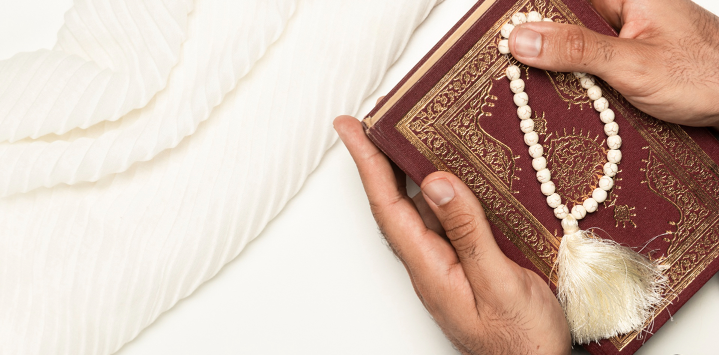 Hands holding the Quran and prayer beads