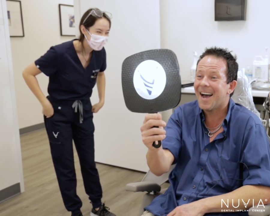 Man looking in mirror and smiling with his new set of teeth