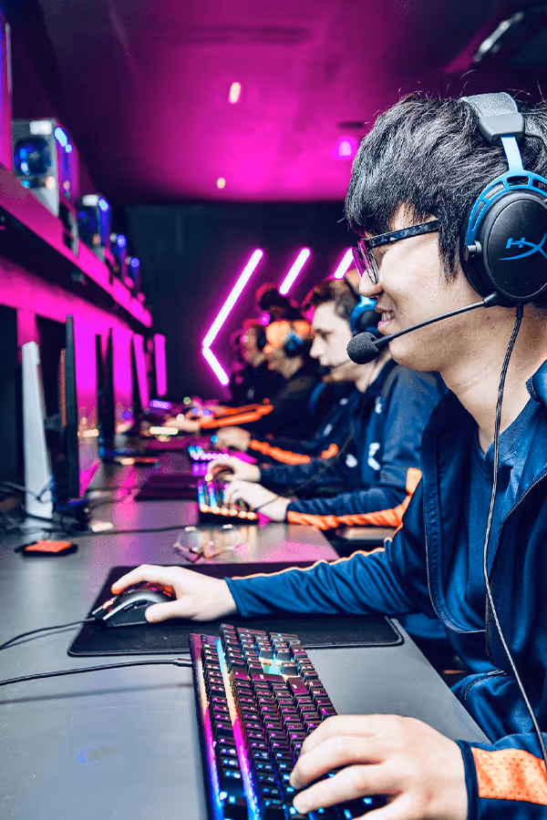Gamers at a gaming station with neon lighting, focused intently on their screens, wearing headphones and using high-end gaming equipment.