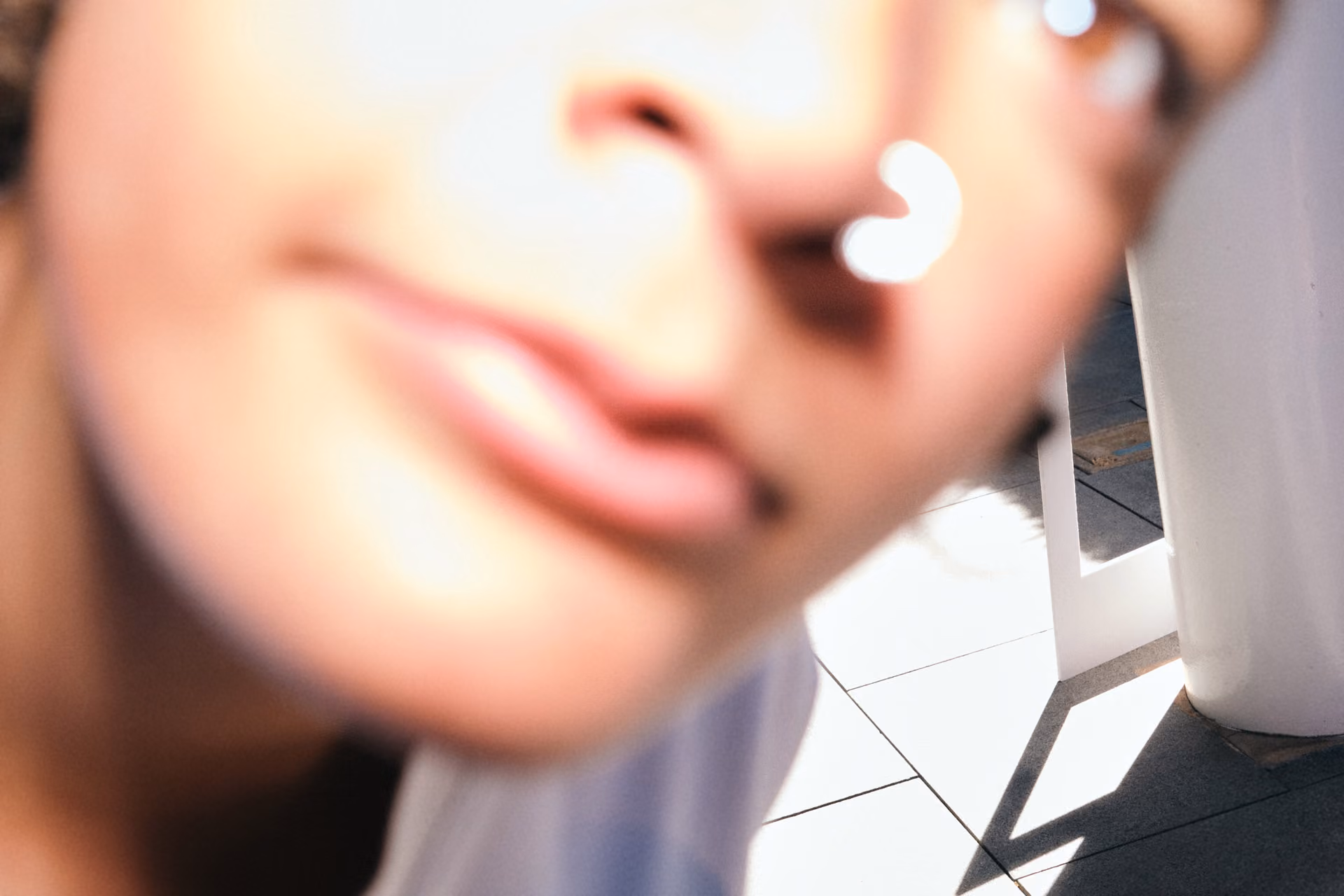Close-up of a person's face with a nose ring and blurred background of tiled floor and white pillar.