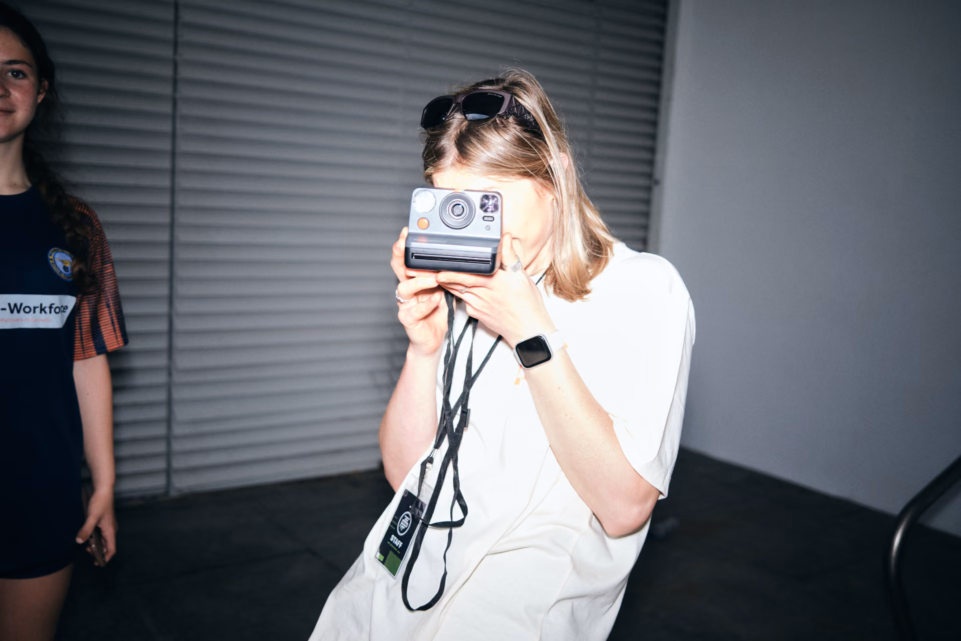 Person in white shirt taking photo with an instant camera indoors at night.