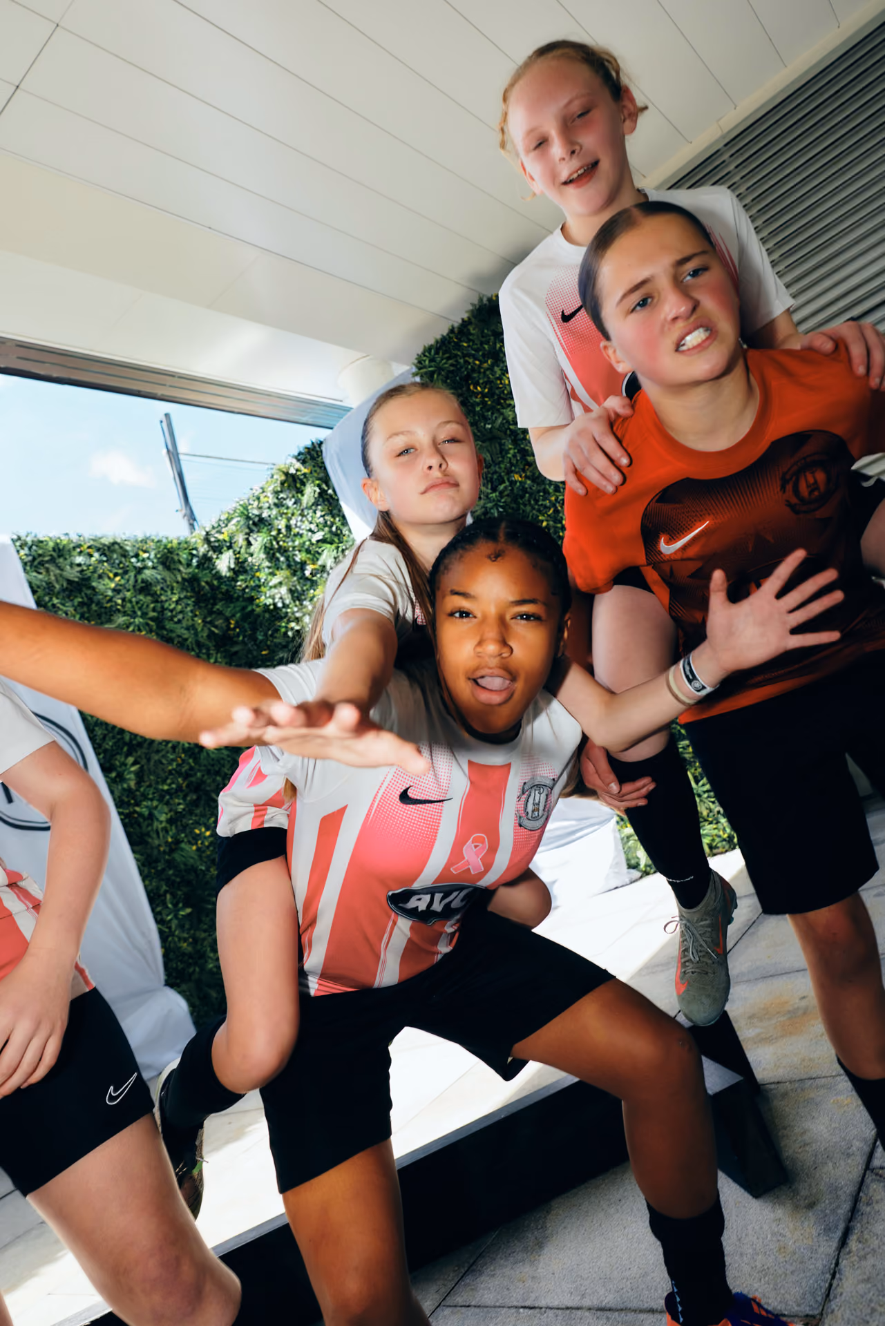 Young soccer players posing energetically outdoors wearing team jerseys in white and orange colors.
