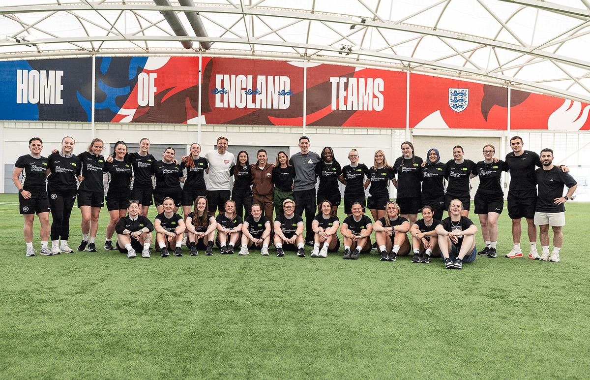 Large group of young female soccer players and coaches posing on an indoor field with banners.