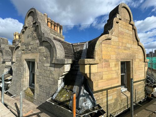 Two ornate stone gables with windows on a historic building under blue sky with scattered clouds.