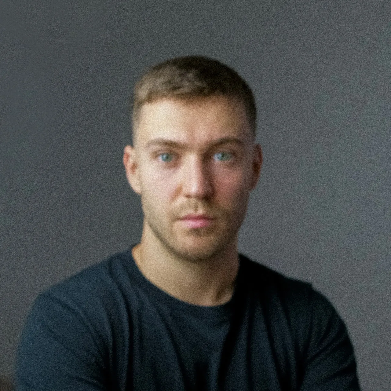 Man with short light hair in a dark shirt, neutral background.