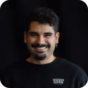 Smiling man with dark hair and beard on a black background.