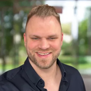 Headshot of a man smiling in front of a leafy, blurred background.