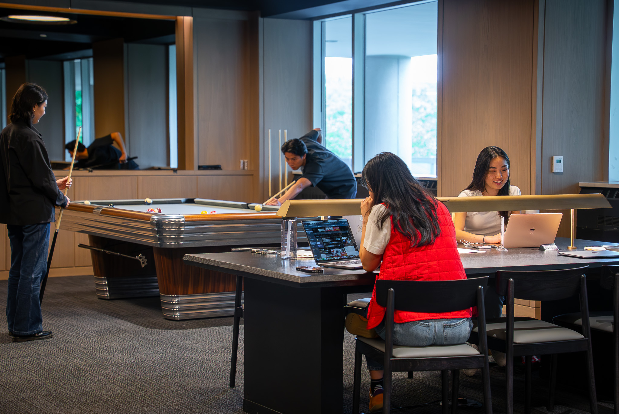Members taking a break from their work day to play pool. People using their laptops in the coworking area at FIELDHOUSE gym