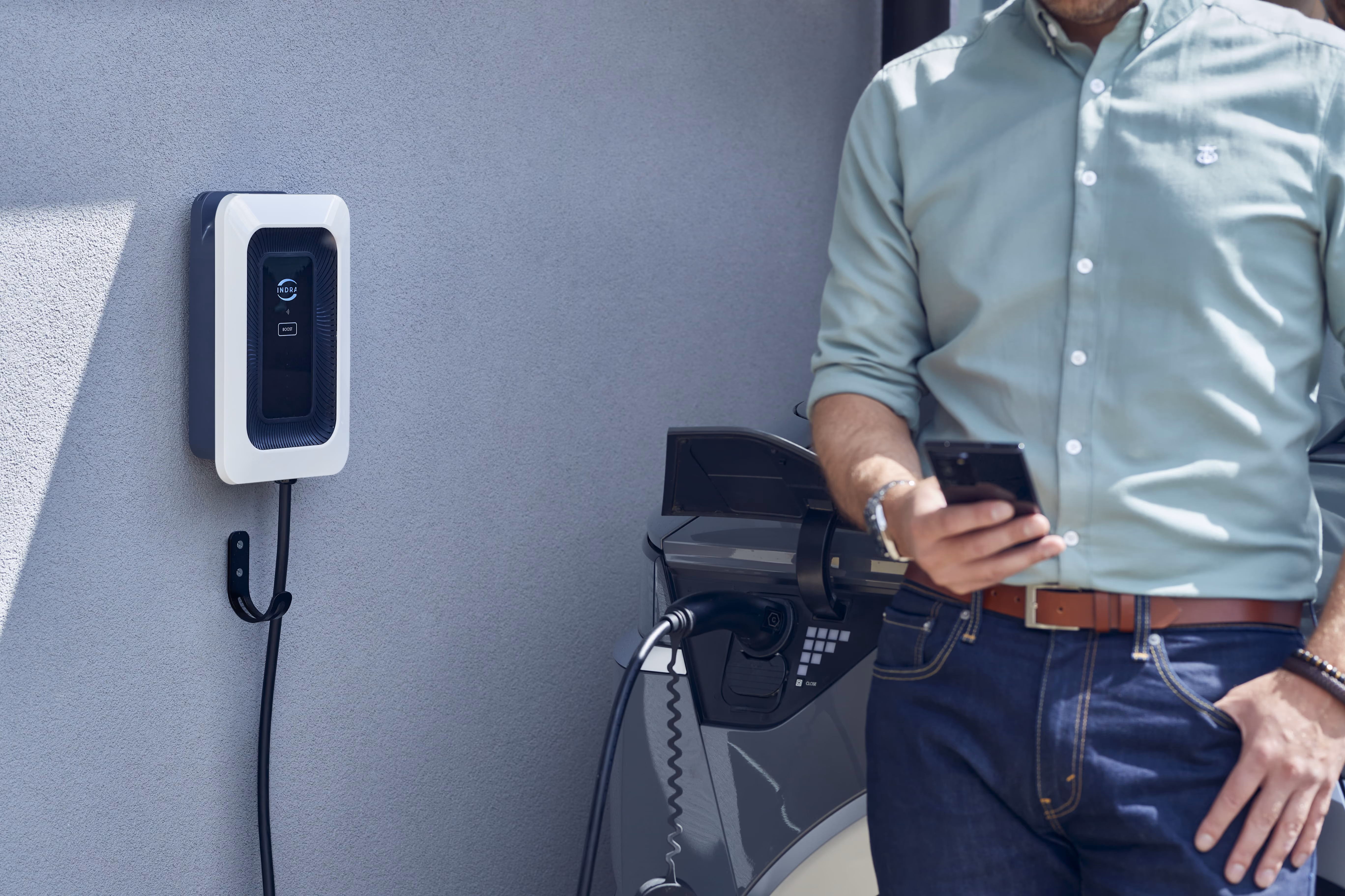 indra home charger on the wall and a person holding a smartphone