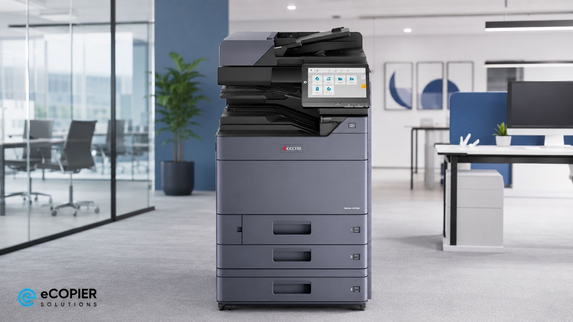 A large Kyocera multifunction office copier stands in the center of a modern business workspace with multiple paper drawers, an automatic document feeder, and a touchscreen control panel. The machine is positioned on gray carpet beside glass-walled meeting rooms and open office desks with computer monitors. A tall indoor plant, minimalist wall art, and blue office partitions add to the clean corporate setting. The scene presents the copier as a professional solution for high-volume printing, scanning, and copying in an office environment.
