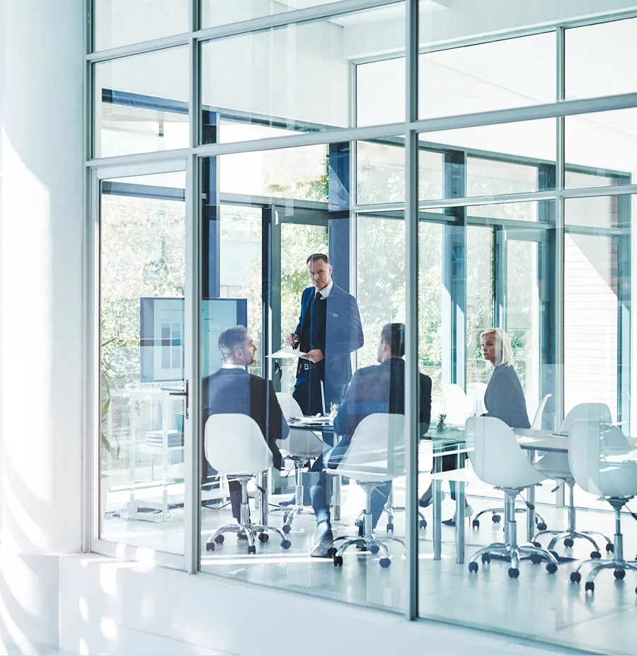 Business team having a meeting in a modern glass conference room with a man standing and presenting.