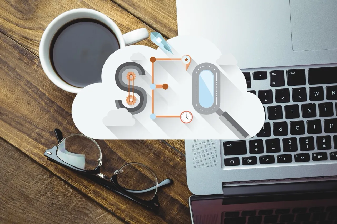 Une tasse de café, des lunettes et un ordinateur portable avec un nuage illustrant le SEO au centre.