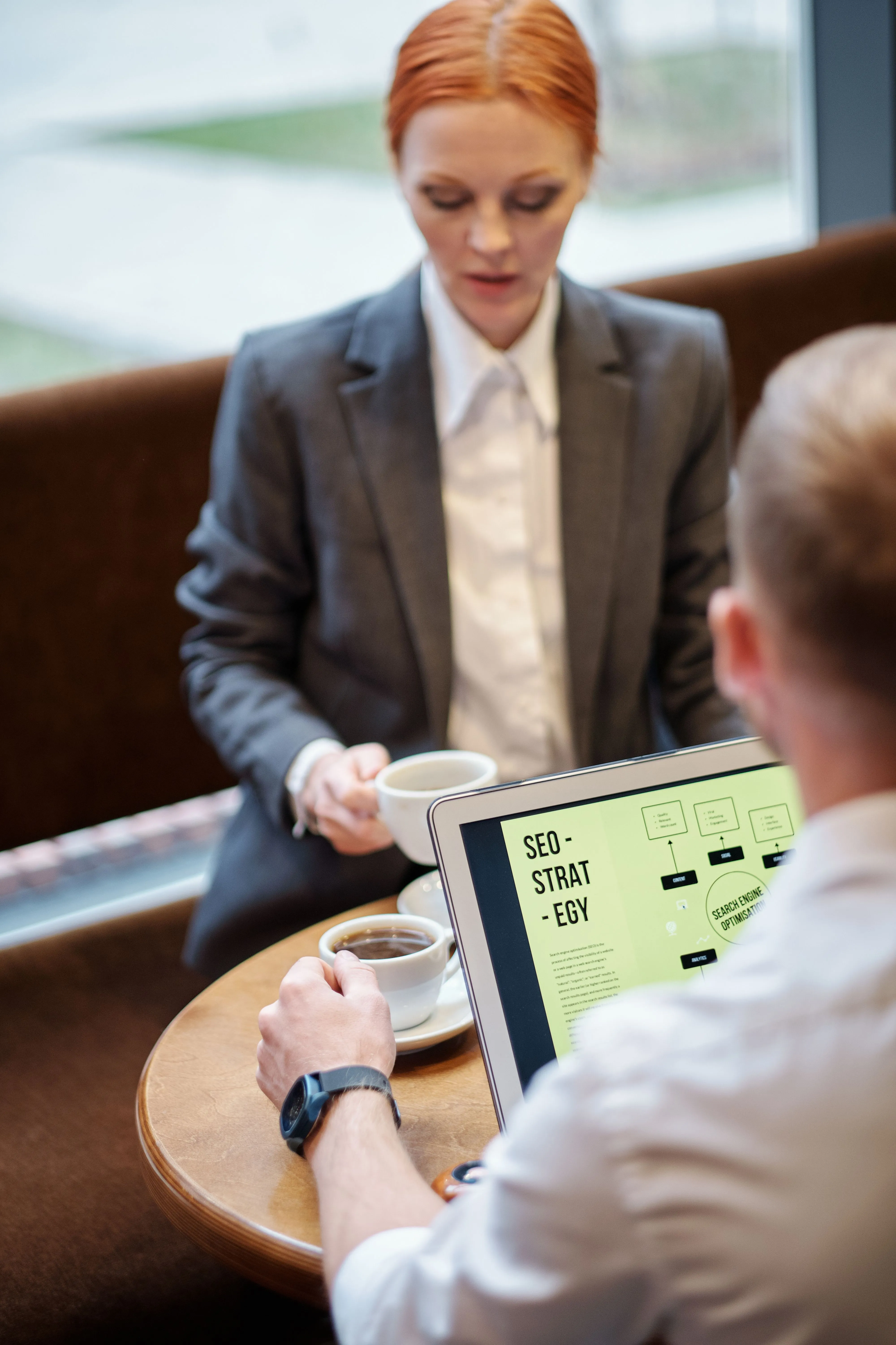 Deux professionnels en réunion café, l'homme consulte la stratégie SEO sur son ordinateur portable.