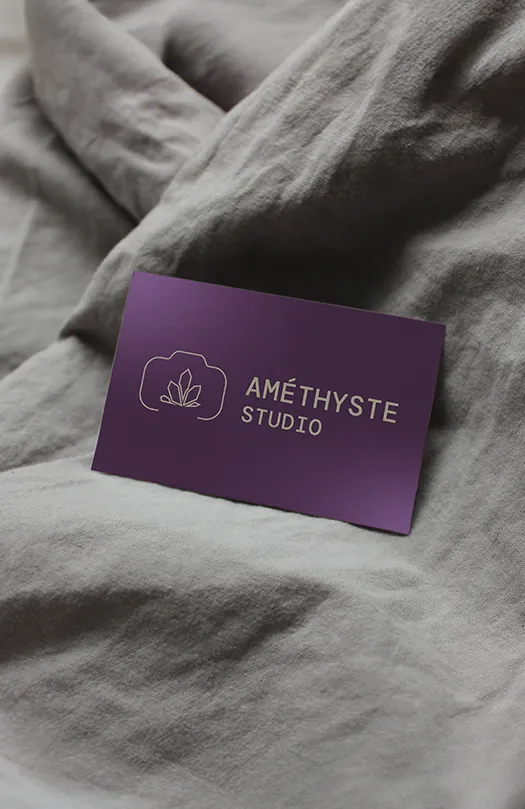 Carte violette Améthyste Studio avec logo minimaliste posée sur tissu gris froissé.
