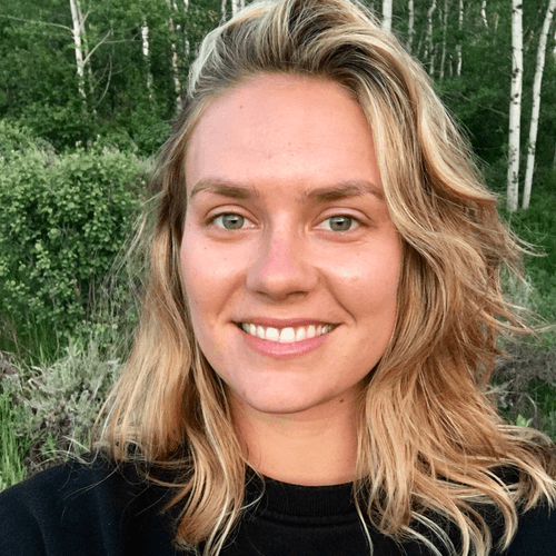 Smiling young woman with blonde wavy hair outdoors with green foliage in background