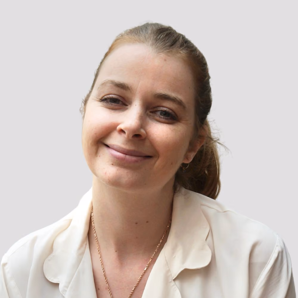 Smiling woman with light skin and brown hair pulled back wearing a cream blouse and gold necklace.
