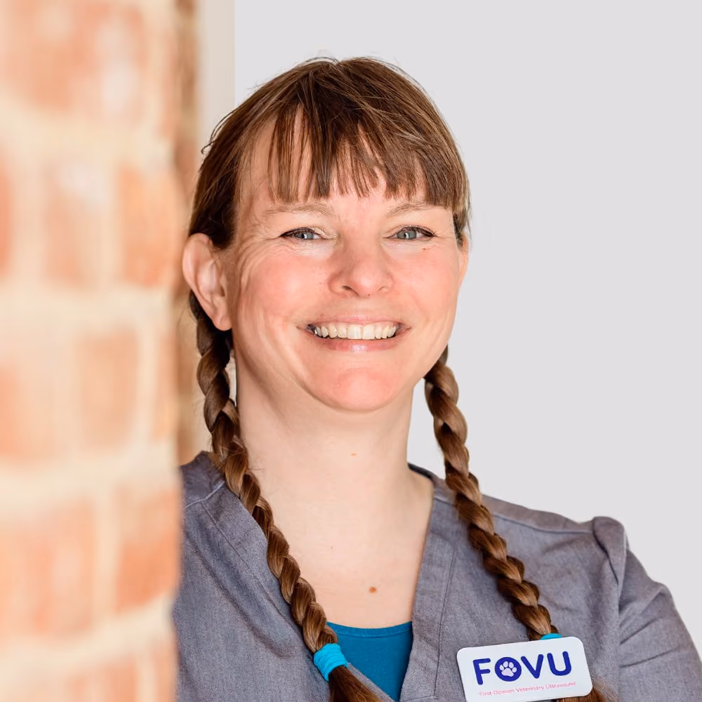 Smiling woman with braided hair in a gray uniform with FOVU veterinary badge.