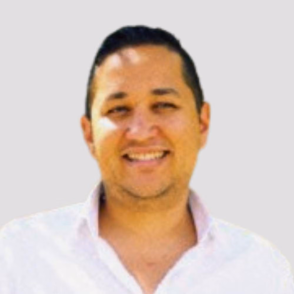 Smiling man with short dark hair wearing a white collared shirt against a plain background.