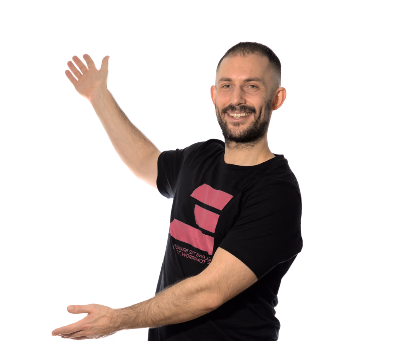 Smiling man with short beard wearing a black t-shirt, gesturing with both hands as if holding something.