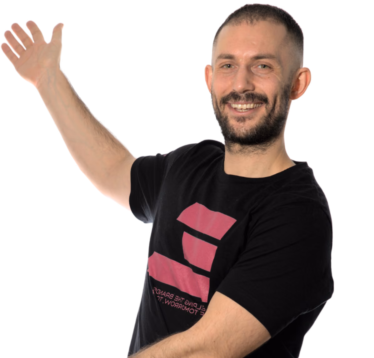 Smiling man with beard and short hair raising left hand in a black t-shirt with a pink design.