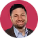 Smiling man with beard wearing a suit jacket and white shirt on a pink background.