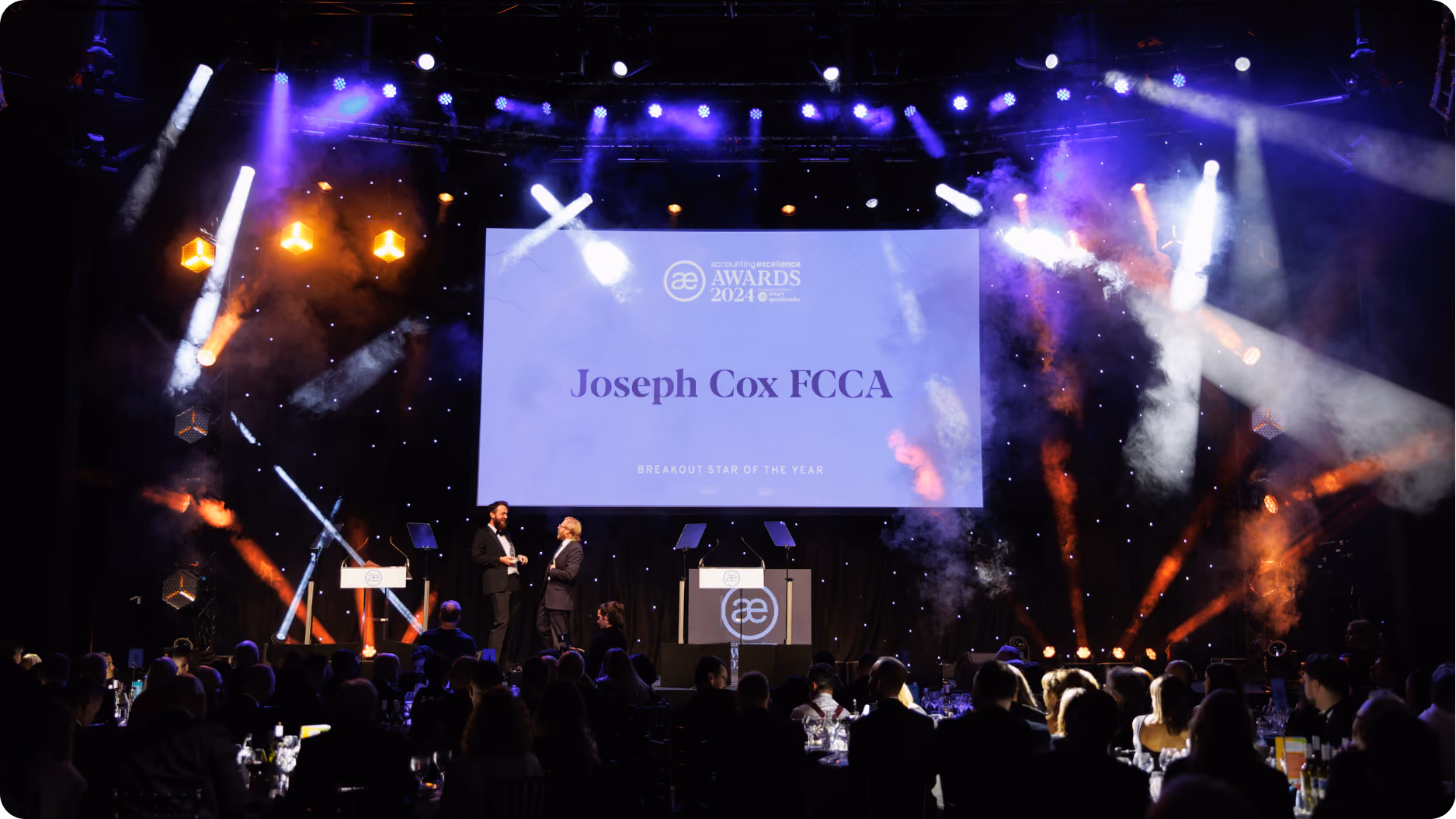 Awards ceremony stage with spotlight on Joseph Cox FCCA, breakout star of the year, with seated audience.
