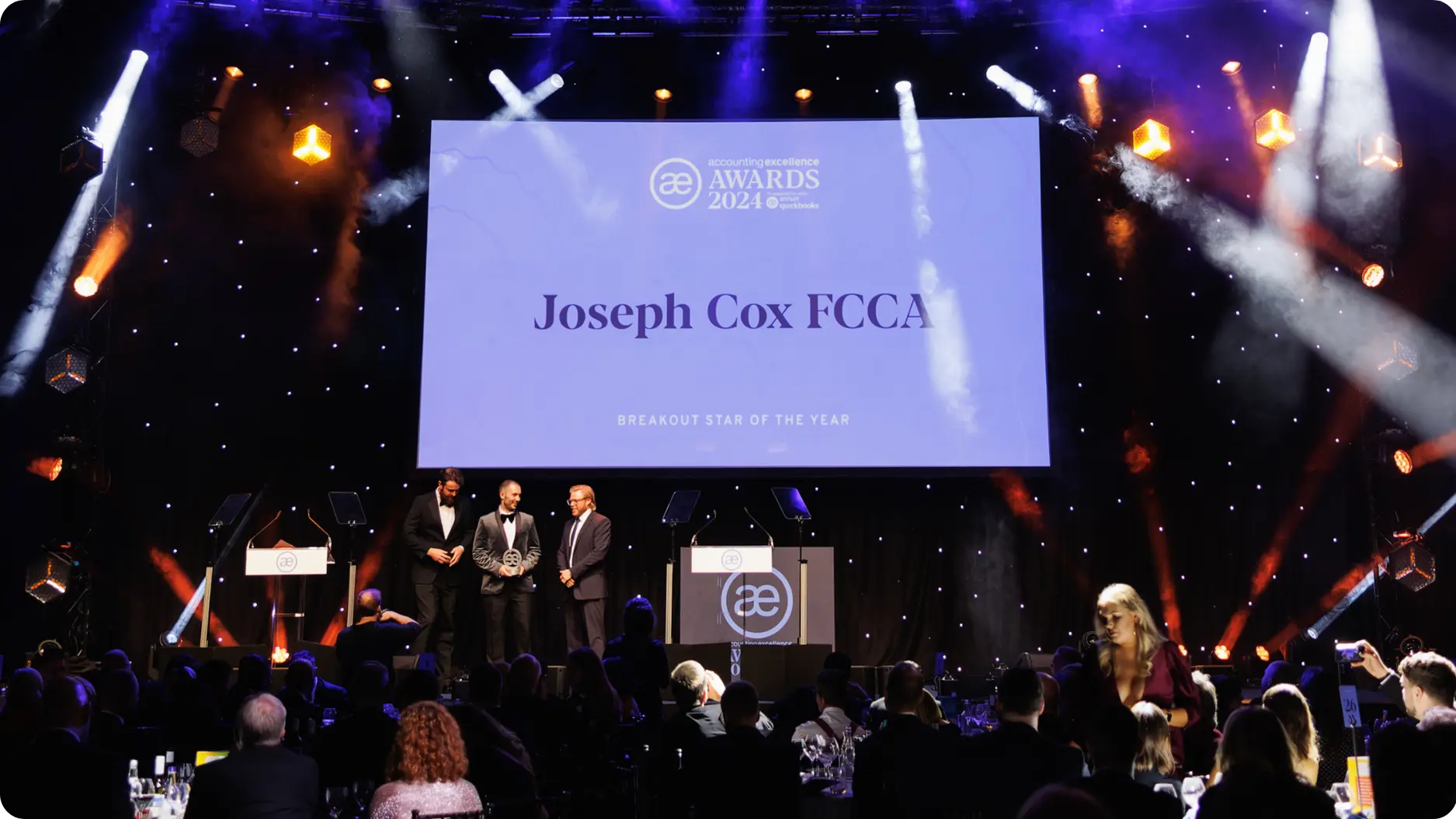 Awards ceremony stage with spotlight on Joseph Cox FCCA, breakout star of the year, and audience seated.