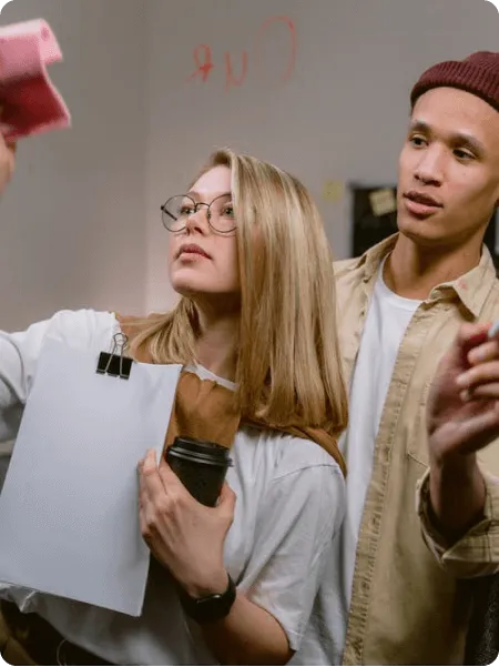 Deux jeunes adultes collaborant, une femme tenant un carnet à spirale et un café, un homme la regardant avec attention.