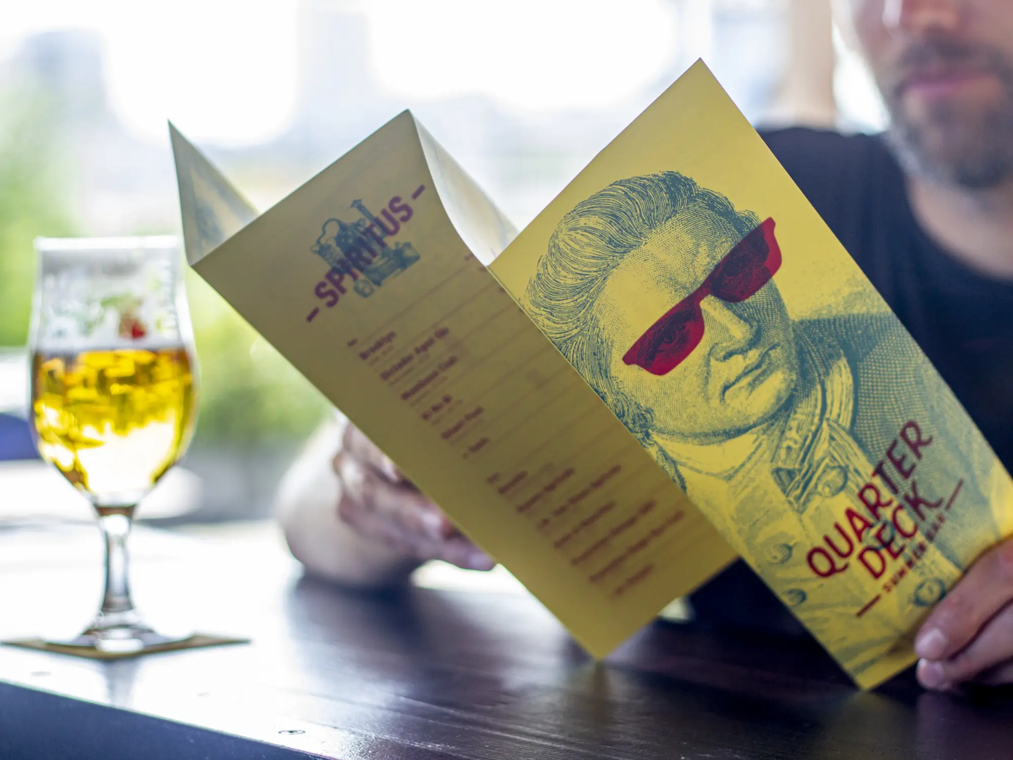 Jemand schaut sich das Quarterdeck Menu an. Daneben steht ein volles Bier.