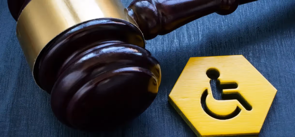 ADA signage compliance concept showing a judge's gavel next to a yellow wheelchair accessibility symbol.