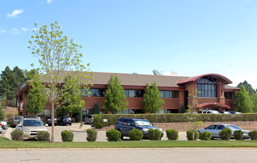 Office building exterior with parking lot, trees, and blue sky, related to DOOH advertising solutions.