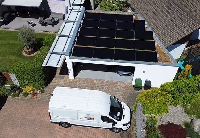 Vogelperspektive eines weißen Hauses mit einer Garage mit Solarmodulen auf dem Flachdach und einem weißen Lieferwagen auf dem gepflasterten Hof.
