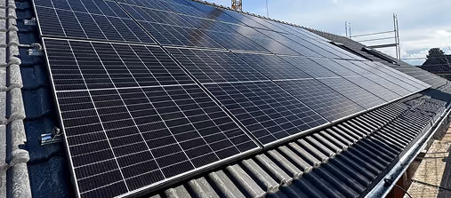 Solarmodule auf einem Dach mit dunklen Ziegeln unter einem bewölkten Himmel.