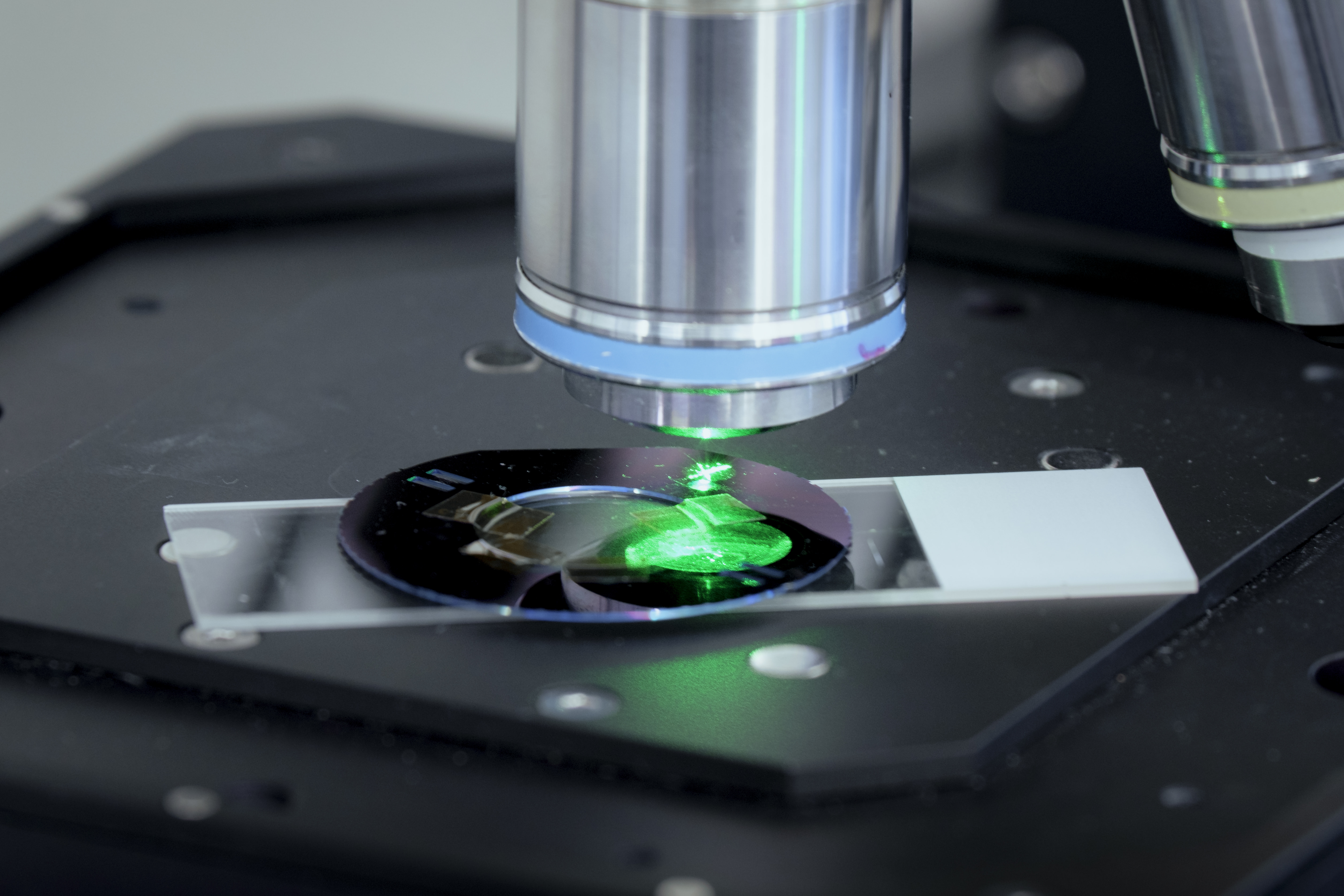 Close-up of a microscope focusing green light on a sample slide in a laboratory setting.