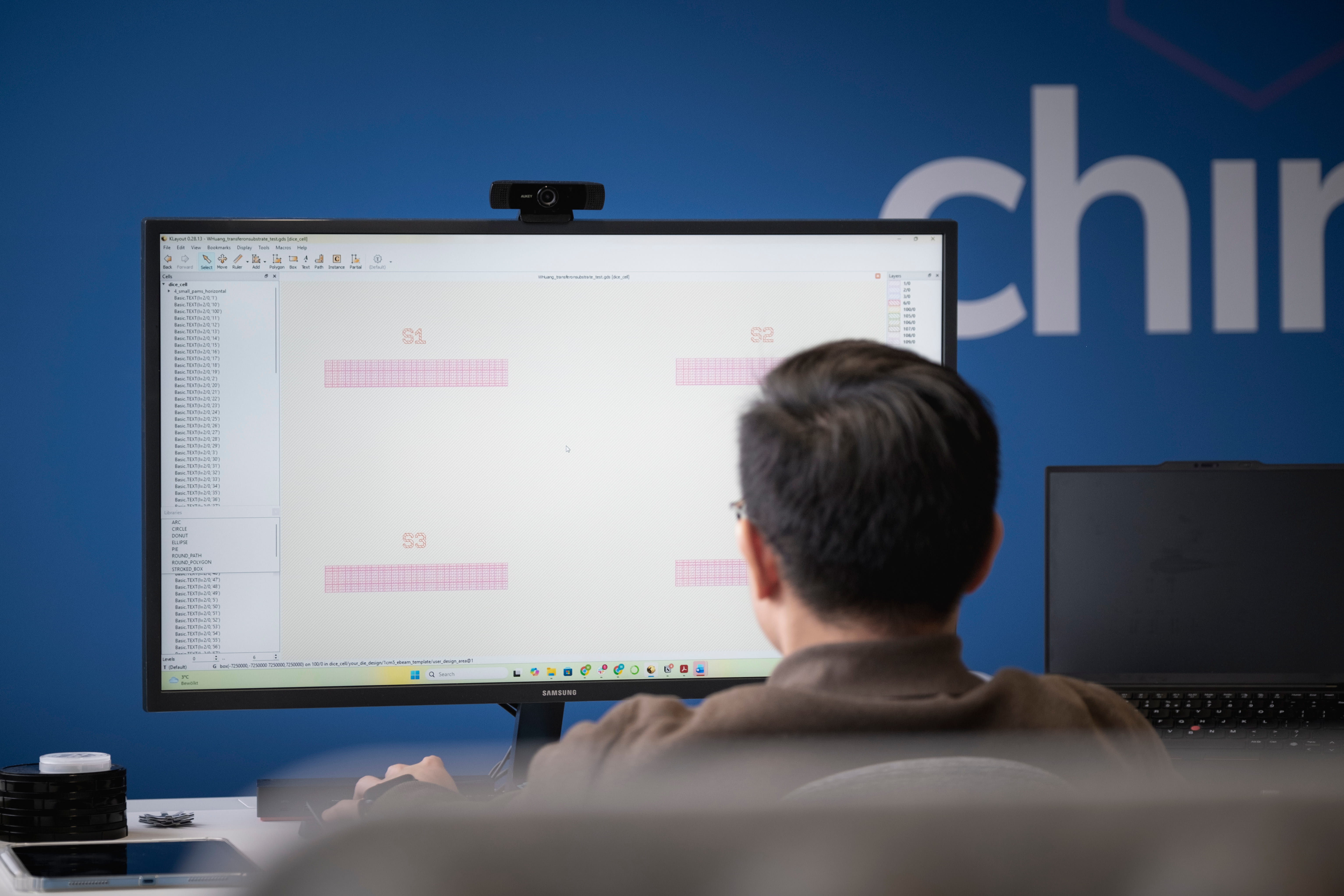 Person working on a desktop computer displaying a software interface with labeled pink grids S1, S2, and S3, seated at an office desk.