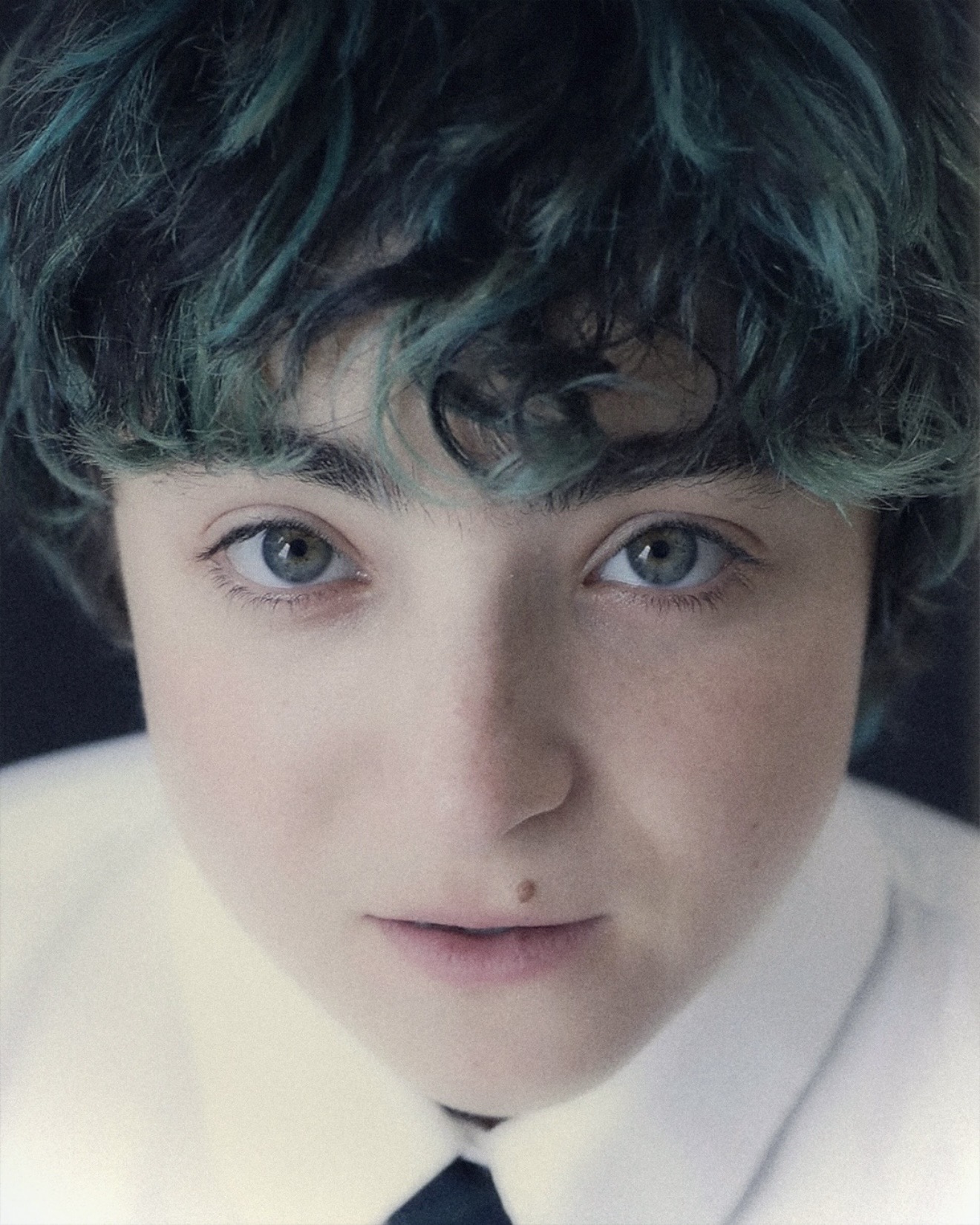 Close-up portrait of Claud with teal-dyed curly hair and a white collar looking directly into the camera, Me and the Music, Dead Oceans, Medicine Box interview 2026