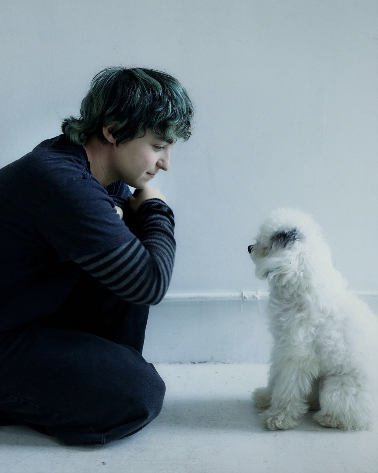 Claud crouching face to face with their white rescue puppy from Animal Haven against a white wall, Me and the Music interview, Medicine Box 2026